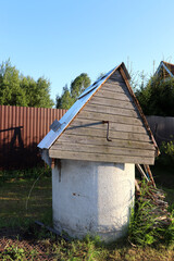 Round stone well for water extraction with a wooden roof in the garden of a rural house. Vertical photo, profile view