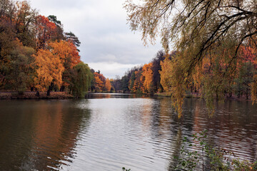 Autumn landscape with lake and colorful trees in city park at cloudy day