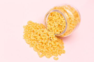Uncooked Chifferi Rigati Pasta in Glass Jar on Pink Background. Fat and Unhealthy Food. Scattered Classic Dry Macaroni. Italian Culture and Cuisine. Raw Pasta