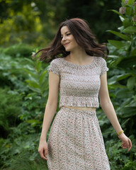 Fototapeta premium Portrait of a beautiful brunette joyful girl in dress posing in the park, tree background. 