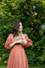 Portrait of a beautiful brunette girl touching a face,  in dress posing in the park, tree...