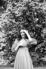 Portrait of a beautiful brunette girl in dress posing in the park, tree background. Black and white photo.
