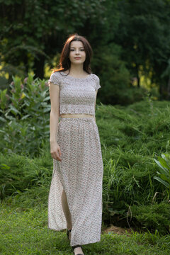 Full length image of a beautiful cute brunette girl in dress posing in the park, tree background.

