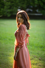 Portrait of a beautiful brunette girl in a slim dress posing in the park, tree background.
