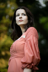 Naklejka premium Profile portrait of a beautiful brunette girl in dress posing in the green park, tree background. 