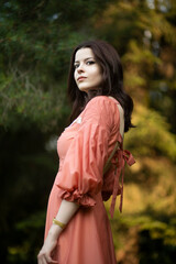 Outside portrait of a beautiful brunette girl in dress posing in the park, tree background.
