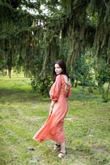 Full length of a beautiful brunette girl in dress posing in the park, tree background.
