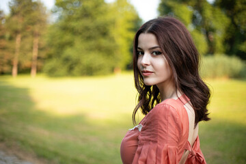 Horizontal view of a beautiful brunette girl in dress posing in the park, tree background. Space for text.
