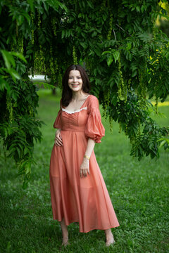 Full length image of a beautiful happy brunette girl in dress posing in the park, tree background.
