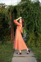 Obraz na płótnie Canvas Full length of a beautiful brunette girl in orange dress posing in the park, green background. 