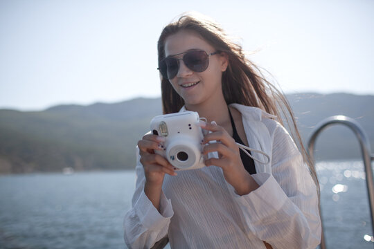 A beautiful girl with a slender figure travels on a boat during a summer vacation in the open sea or ocean against the background of the islands. Female makes photo on camera