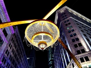 Low angle shot of a lit chandelier on a street with buildings in the background