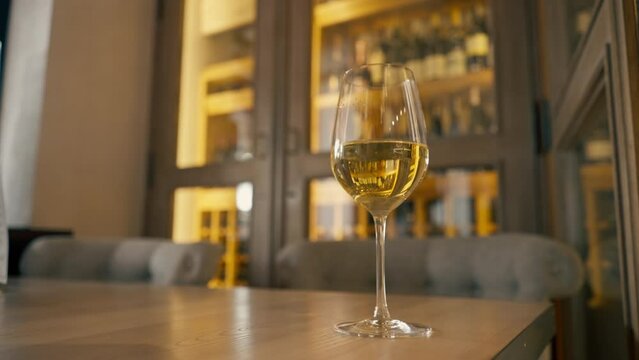 Close-up of a glass of white wine standing on a table in an Italian restaurant against a wine rack