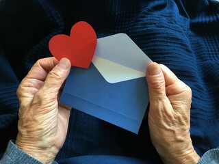 Person holding a red heart and blue envelope
