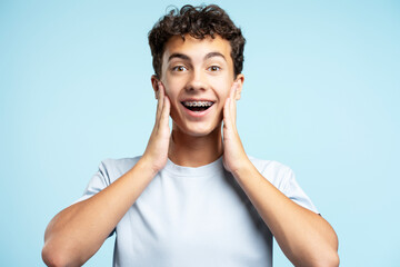 Surprised handsome teenage boy wearing dental braces touching face looking at camera