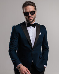 tough elegant groom wearing tuxedo and sunglasses and posing