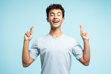 Portrait of smiling handsome young man holding fingers crossed, eyes closed standing