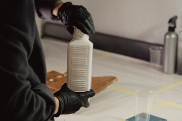 A woman in black protective gloves takes a white bottle with a primer in the workshop. Unscrews the...