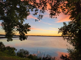 Beautiful view of a calm lake lake surrounded by green vegetation during the purple sunset