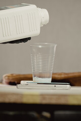 Woman in black protective gloves pours solvent from a white bottle into a plastic cup in car workshop. A plastic cup stands on a scale
