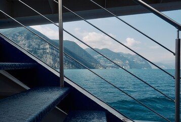 Vista del lago attraverso un parapetto di una nave traghetto con lo sfondo di montagne - obrazy, fototapety, plakaty