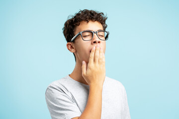 Portrait of tired handsome teenager boy wearing eyeglasses yawning isolated on blue background - obrazy, fototapety, plakaty