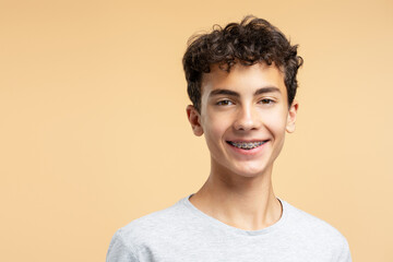 Portrait of smiling handsome boy with braces looking at camera posing isolated on beige background