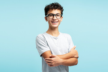 Portrait of smiling attractive teenage boy wearing eyeglasses with crossed arms looking at camera