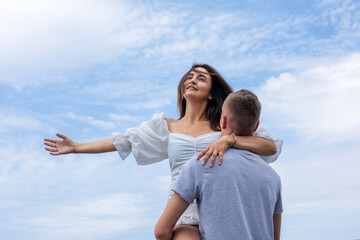 Obraz premium A young guy spins his girlfriend in his arms against the blue sky