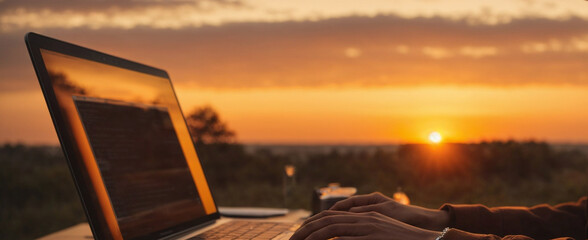Person typing on a laptop against the warm hues of a sunset. Freelance jobs and business concept. Freedom and lifestyle idea. With copy space.