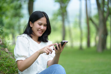 Young female student playing with mobile phone, chatting, sending messages inside a public park