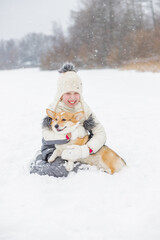 happy child having fun in snowy winter park with Corgi baby dog.Walking the dog in the park in winter. girl plays with corgi. copy space