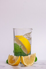 Citrus iced lemonade in pitcher and glasses with lemon slice and mint leaves decoration and on marble table on natural background. Fresh summer drink beautiful picture. Copy space