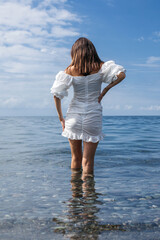A sexy girl with a beautiful figure stands knee-deep in the sea against the blue sky © Krystsina