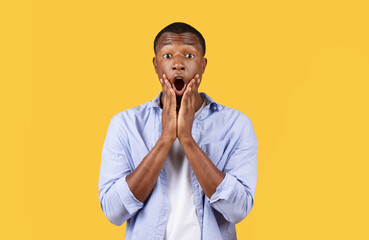 Shocked man with hands on cheeks, yellow background