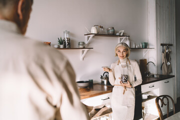 Cheerful aged woman preparing breakfast for husband