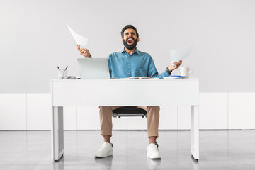 Stressed indian man with papers at office desk