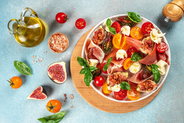 Fresh Salad with mozzarella, figs, prosciutto, fresh basil leaves and tomato on a light background top view