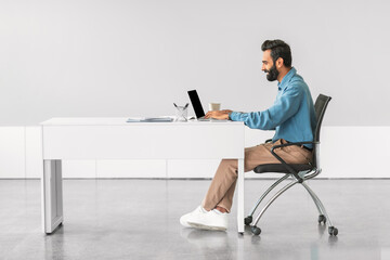 Indian man working intently on computer at desk, side view