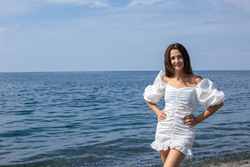 Beautiful brunette stands against the background of the sea, horizontal frame