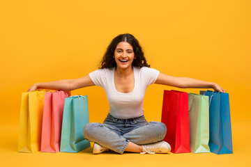 Positive young indian woman shopaholic sitting on floor with purchases