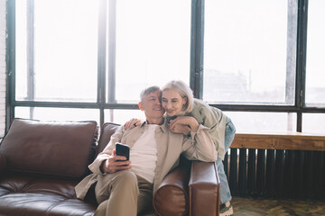 Obraz premium Senior couple using smartphone on sofa