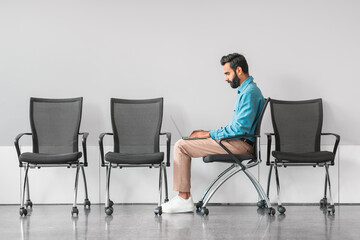 Focused indian man working on laptop in waiting area, side view