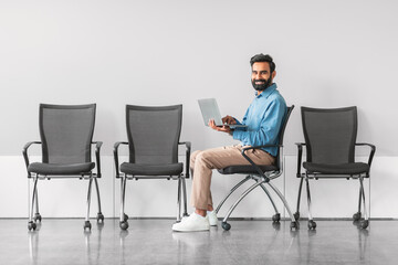 Cheerful indian man with laptop in waiting room