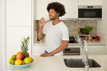Happy black man sipping water amidst food prep at kitchen