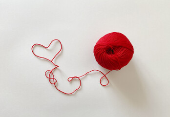 Red wool yarn on a white background. The thread is twisted in the shape of a heart.