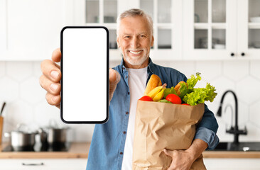 Happy Senior Man Demonstrating Blank Smartphone And Holding Bag With Groceries