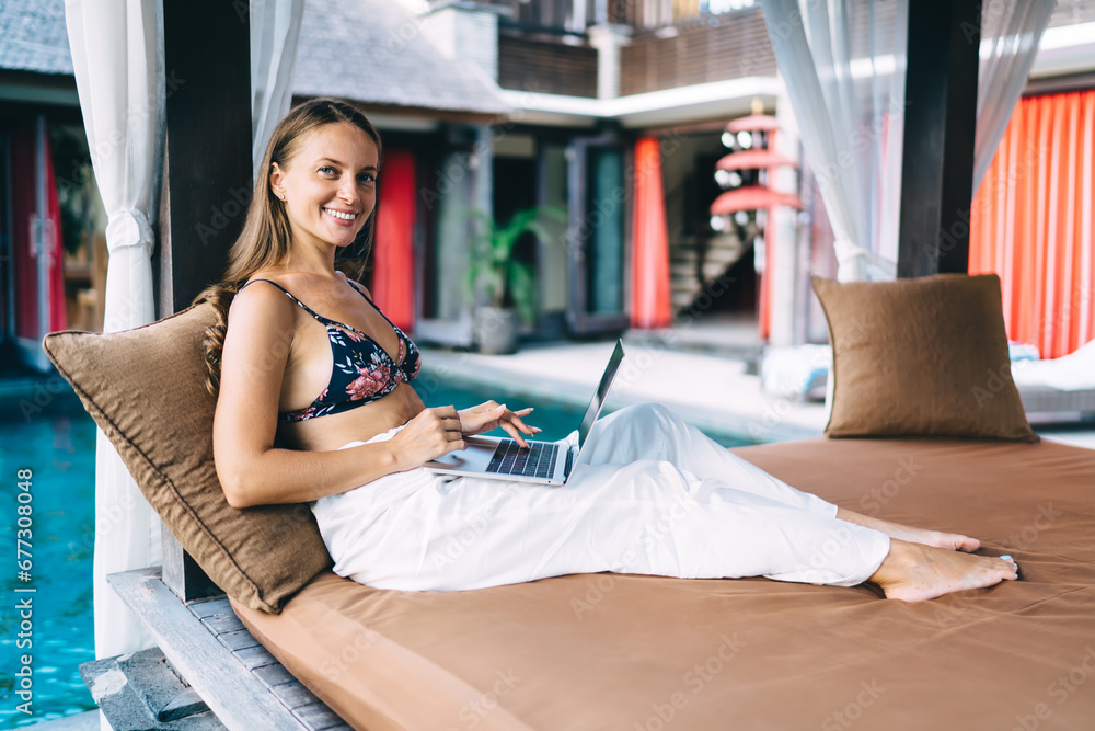 Poster smiling woman using netbook near swimming pool at resort