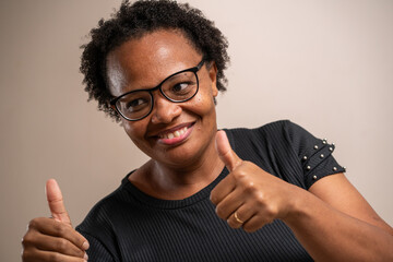 Black woman wearing glasses and smiling with thumbs up on pastel background.