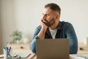 Depressed middle aged man sits troubled at laptop in office